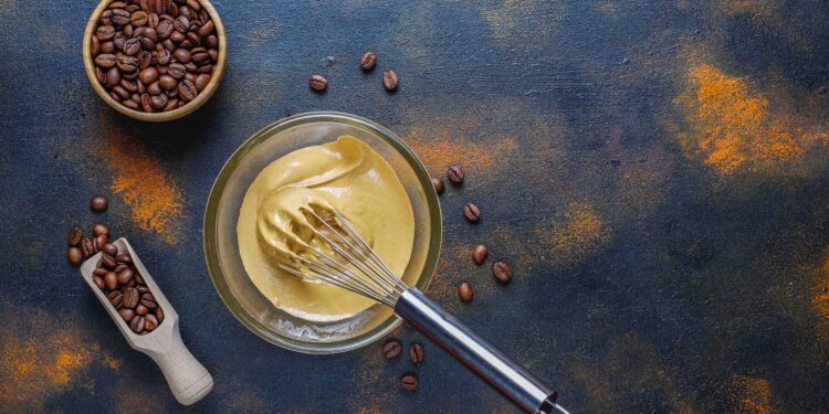 A imagem apresenta grãos de café, um recipiente de vidro e um fouet.